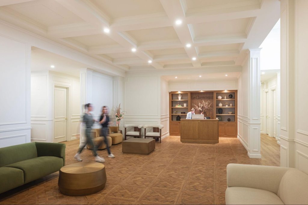 Salle d’accueil élégante de la clinique Le Clayemont à Montréal, avec réception en bois, mobilier haut de gamme, éclairage chaleureux et espace d’attente spacieux offrant une expérience médicale et médico-esthétique raffinée.